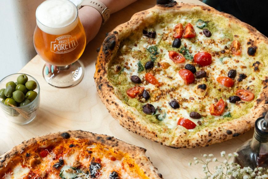 two pizzas, a beer and a bowl of olives on a table